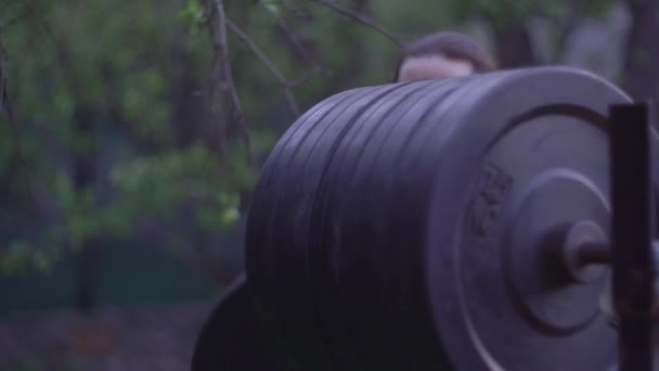 Um atleta masculino prepara uma barra para treinamento, um simulador de esportes no pátio — Vídeo de Stock