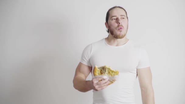 Hombre atlético con barba roja, con una camiseta blanca sobre fondo blanco, come pan con carne, khachapuri — Vídeos de Stock