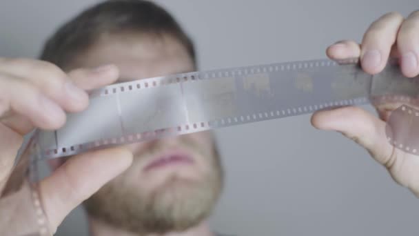 一个留着胡子的金发男人，一个摄影师，用白色背景来审视一部电影 — 图库视频影像