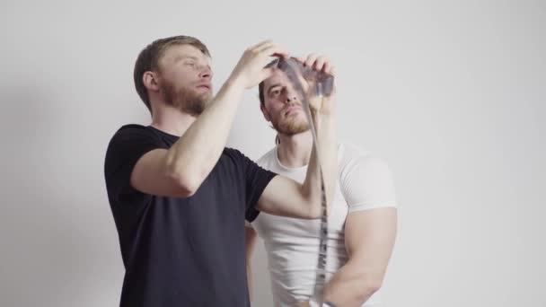 Two guys are standing in a white room, looking at the filmstrip — Stock Video