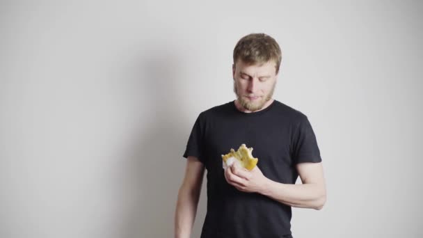 Un ragazzo magro con una maglietta nera, mangia un panino Un uomo sportivo con la barba rossa, con una maglietta bianca, lo vergogna per un'alimentazione impropria e gli dà una banana. — Video Stock