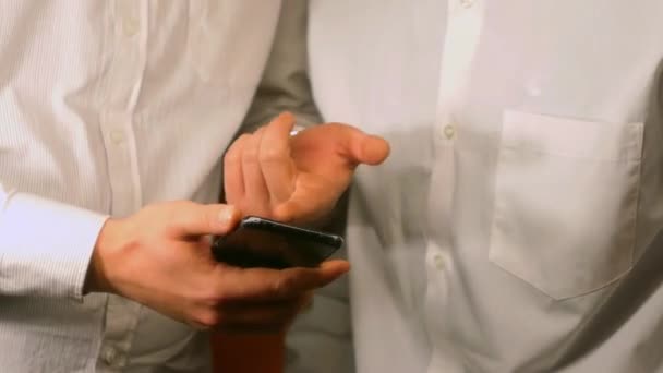 Dwóch Mężczyzn Białych Koszulach Patrzy Nową Aplikację Smartfonie Przewijam Strony — Wideo stockowe