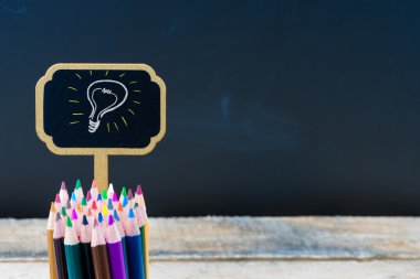 Wooden mini blackboard label with light bulb as idea and colouring pencils over chalkboard background