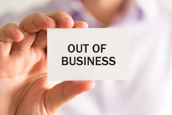 Businessman holding card with text OUT OF BUSINESS — Stock Photo, Image