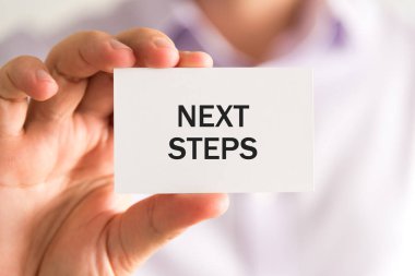 İş adamı elinde NEXT STEPS yazılı bir kart tutuyor