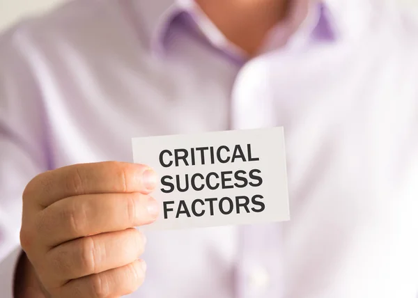 Businessman holding a card with text CRITICAL SUCCESS FACTORS