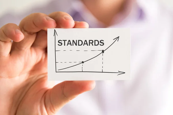 Businessman holding a card with STANDARDS rising arrow and chart — Stock Photo, Image