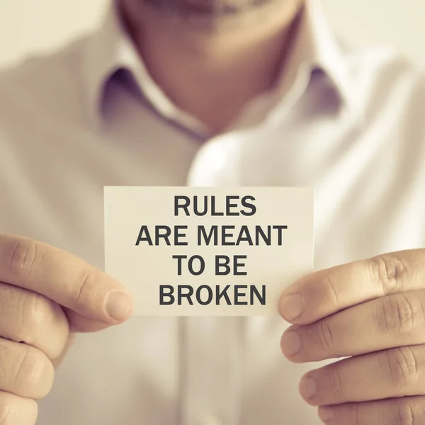Businessman holding RULES ARE MEANT TO BE BROKEN message card
