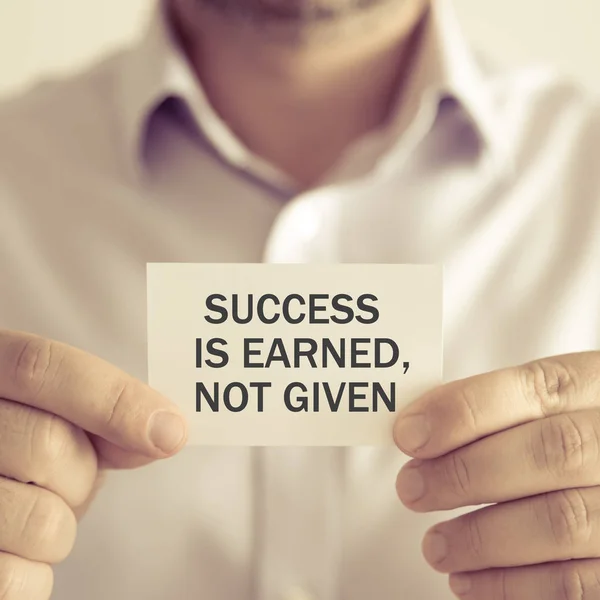 Businessman holding SUCCESS IS EARNED, NOT GIVEN message card — Stock Photo, Image