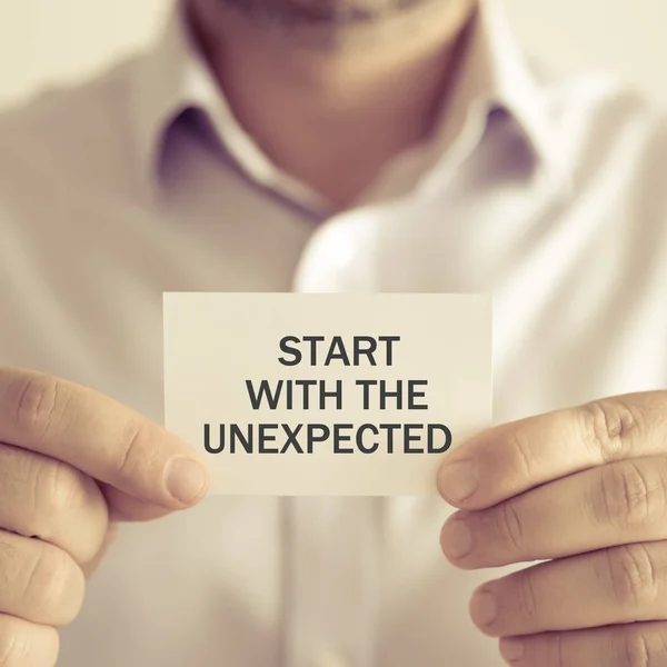 Businessman holding START WITH THE UNEXPECTED message card — Stock Photo, Image