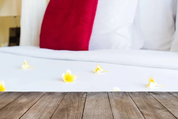 Perspective empty wooden table in front of hotel bed with flowers — Stock Photo, Image
