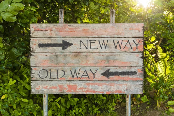 Old Way versus New Way with directional arrows on old vintage board sign in the forrest, with sun rays in background. — Stock Photo, Image