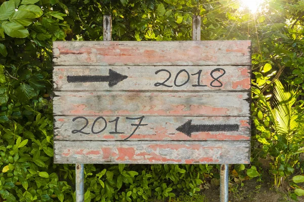 Año 2017 versus 2018 con flechas direccionales en el antiguo letrero de madera vintage en el bosque, con rayos de sol en el fondo . — Foto de Stock