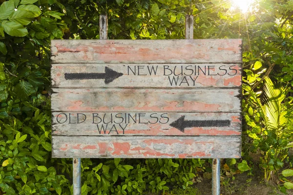 Old Business Way contro New Business Way con frecce direzionali sul vecchio cartello vintage nel bosco, con raggi di sole sullo sfondo . — Foto Stock