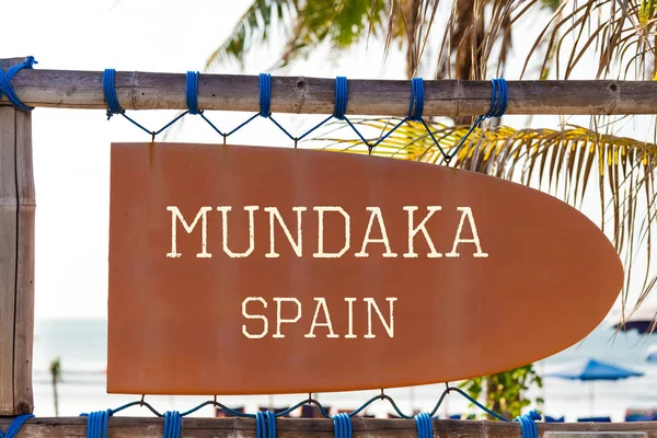 Orange vintage signboard in shape of surfboard with Mundaka Spain text for surf spot and palm tree in background — Stock Photo, Image