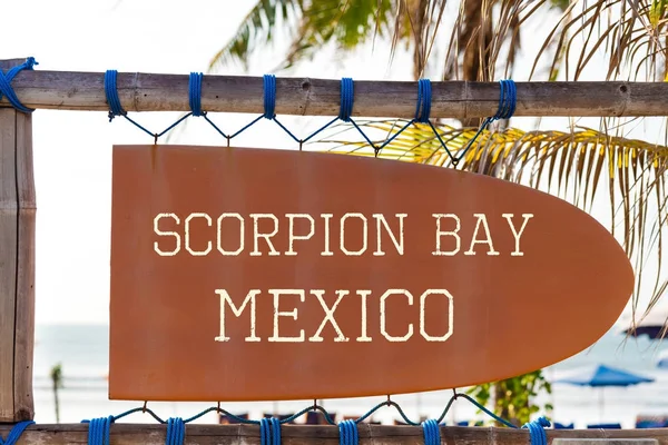 Orange vintage signboard in shape of surfboard with Scorpion Bay Mexico text for surf spot and palm tree in background — Stock Photo, Image