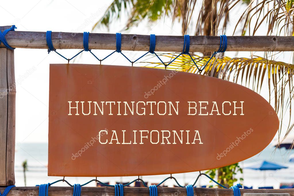 Orange vintage signboard in shape of surfboard with Huntington Beach, California text for surf spot and palm tree in background