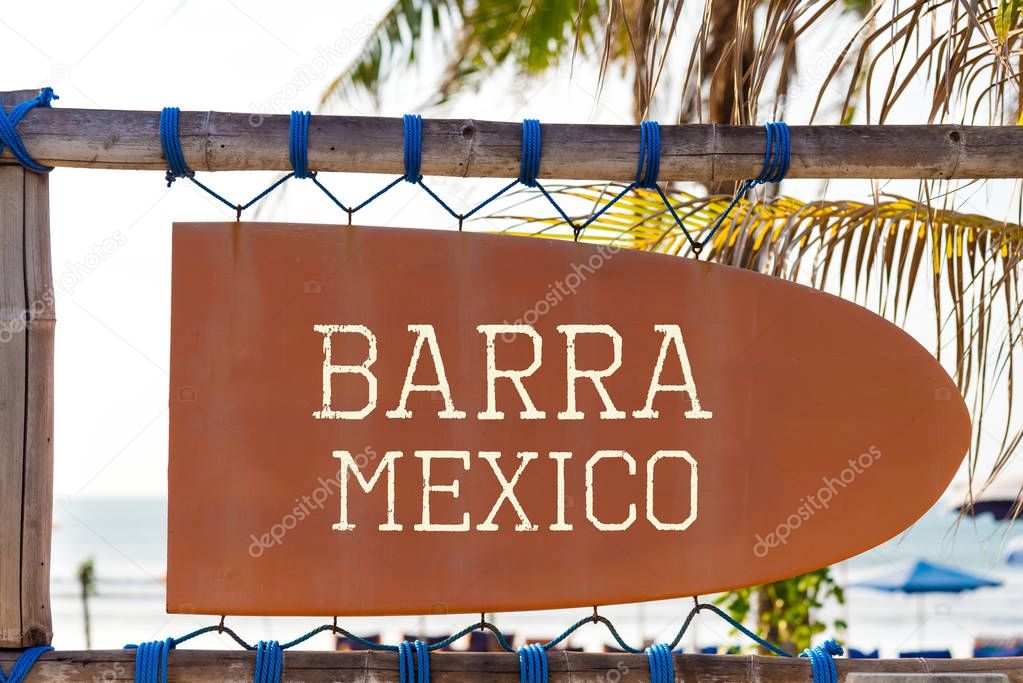 Orange vintage signboard in shape of surfboard with Barra Mexico text for surf spot and palm tree in background