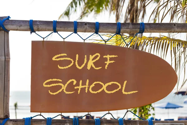 Orange vintage signboard in shape of surfboard with Surf School text and palm tree in background — Stock Photo, Image