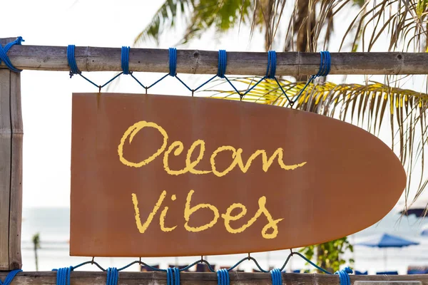 ป้ายสีส้มวินเทจในรูปของกระดานโต้คลื่นที่มีข้อความ Ocean Vibes และต้นปาล์มในพื้นหลัง — ภาพถ่ายสต็อก