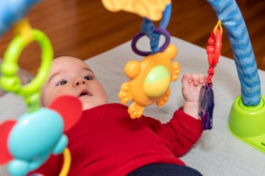 Sırtüstü yatmış 6 aylık sevimli bir oğlan çocuğu. Etrafı renkli oyuncaklarla çevrili.