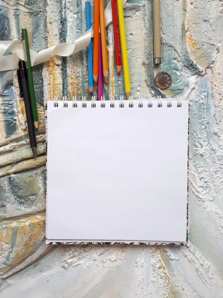 Foto de bloc de notas sobre el fondo de una pared en relieve con lápices de color y otros elementos decorativos — Foto de Stock