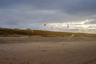 Sahilde ufukta üç paraşütçü uçuyor.