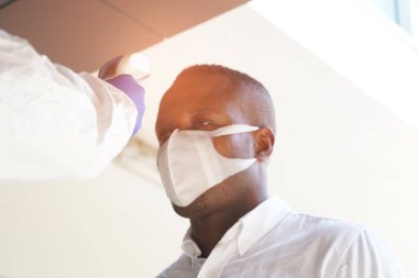 Hastalık kontrol uzmanları, Alnındaki sıcaklığı ölçmek için kızılötesi termometre cihazı kullanır ve binaya girmeden önce Covid bağımlısı hastaları görüntülemek için alkol jeli kullanır..