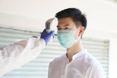 Hastalık kontrol uzmanları, Alnındaki sıcaklığı ölçmek için kızılötesi termometre cihazı kullanır ve binaya girmeden önce Covid bağımlısı hastaları görüntülemek için alkol jeli kullanır..