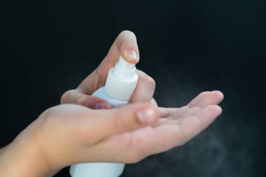 El hijyeni. Bir genç elinde antiseptik tutuyor. Siyah arka plandaki virüse karşı korumak için.