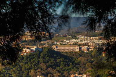 Üniversiteyle birlikte tepeden Malaga 'nın ilçesine bakın. Güneşli bir günde orman ve ağaçlarla kaplı tepeler. Köyde binaları olan bir üniversite.