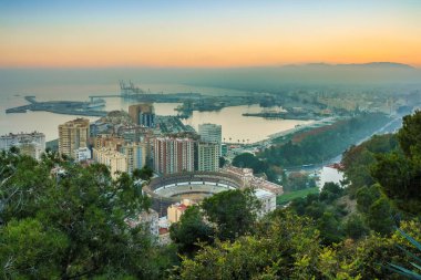 Akdeniz kıyısındaki İspanyol şehri Malaga 'nın üzerinde akşam güneşi. Costa del Sol 'daki şehir merkezinin ışıklandırılmış binalar, ağaçlar, sokak lambaları, liman, gemileriyle görüntüsü