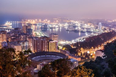 Geceleri İspanya 'nın Akdeniz kıyısındaki Malaga' ya bakın. Şehrin Costa del Sol 'daki panoramik manzarası aydınlık liman, konut binaları, ağaçlar, sokak lambaları, dönme dolap, gemiler...