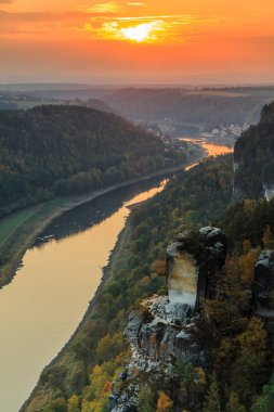 Akşamları Elbe Vadisi ile Sakson İsviçre 'de manzara. Bastei Köprüsü manzaralı ulusal park Elbe ve kayalar, ağaçlar ve ormanlar sonbahar havasında ve gün batımında turuncu bir ufuk ile