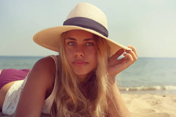 Flickan i hatten ligger på stranden nära havet. — Stockfoto