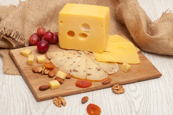 Queso sobre una tabla de madera con uvas, nueces, albaricoques secos —  Fotos de Stock