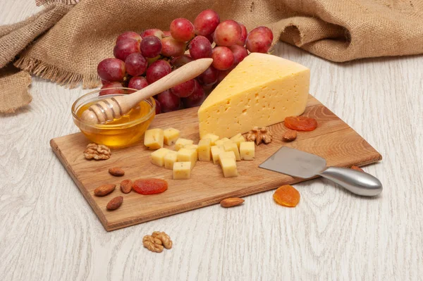 Cheese on a board with honey, grapes, dried apricots and nuts — Stock Photo, Image
