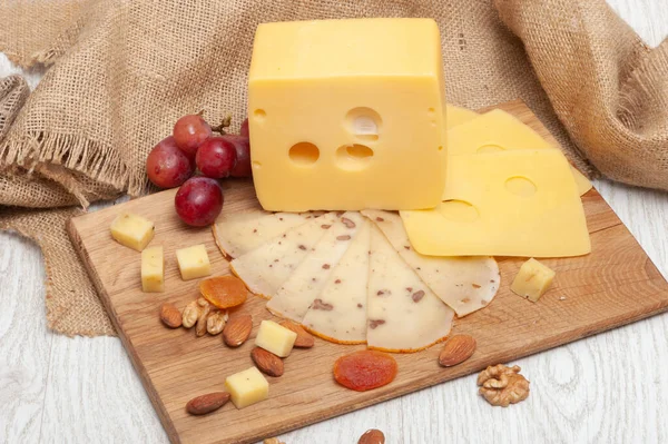 Rebanadas Diferentes variedades de queso en el tablero, uvas, albaricoques secos y frutos secos —  Fotos de Stock