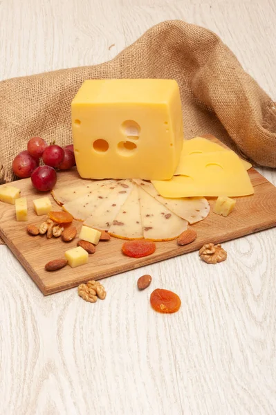 Různé druhy sýrů na tabuli, hrozny, sušené meruňky a ořechy — Stock fotografie