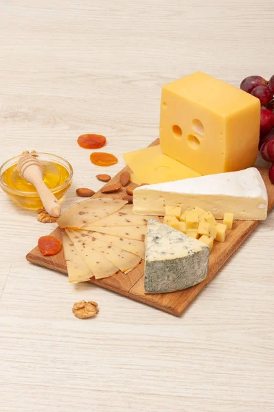 Différents types de fromage avec des noix et des abricots secs, des raisins et du miel sur une planche de bois. Vue du dessus — Photo