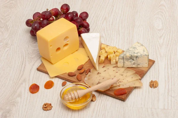 Diferentes tipos de queso con nueces y albaricoques secos, uvas y miel en una tabla de madera. Vista superior —  Fotos de Stock