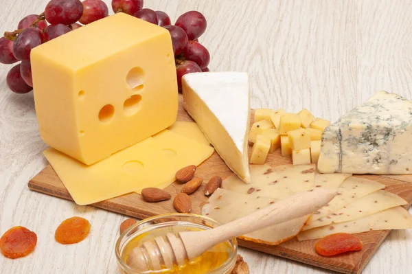 Diferentes tipos de queso con nueces y albaricoques secos, uvas y miel en una tabla de madera. Vista superior —  Fotos de Stock