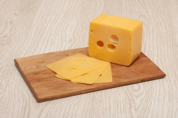 Pedaço de queijo e queijo fatiado em uma tábua de madeira — Fotografia de Stock