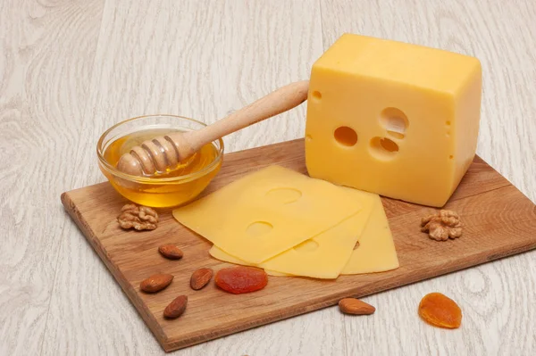 Pedazo de queso y queso en rodajas en una tabla de madera con miel, nueces y albaricoques secos. Vista superior —  Fotos de Stock