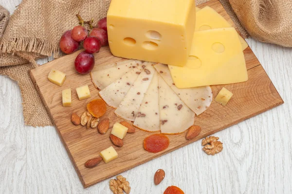 El queso de nuez en rodajas en la tabla, las uvas, los albaricoques secos y los frutos secos —  Fotos de Stock
