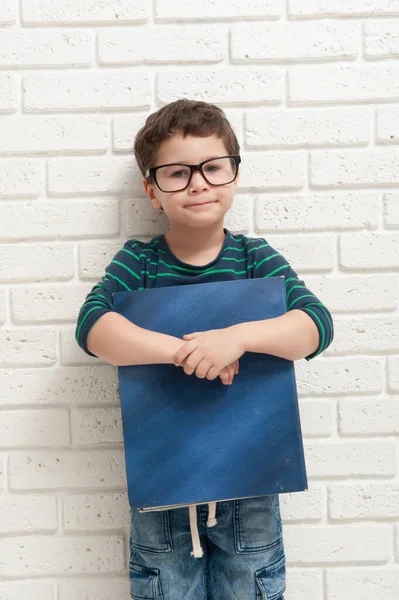 Niño en gafas con un libro sobre un fondo de una pared de ladrillo blanco — Foto de Stock