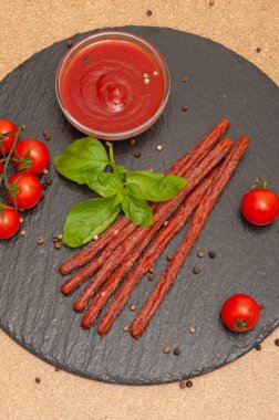 Sosu olan ince uzun sosis, siyah grafit tahtasında kiraz domatesleri ve fesleğen.