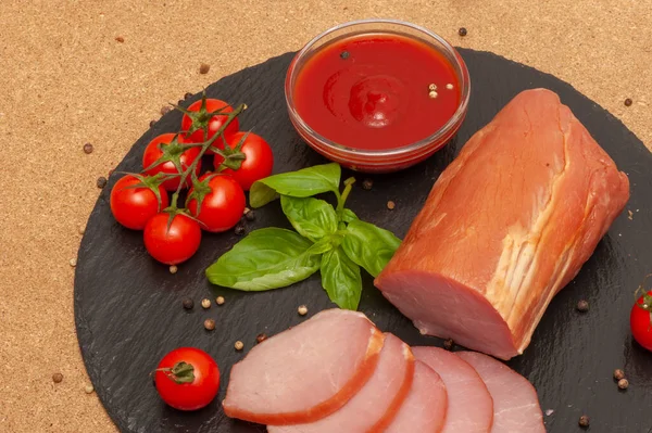 Studené uzené maso s omáčkou, cherry rajčaty a bazalkou na černé grafitové desce — Stock fotografie