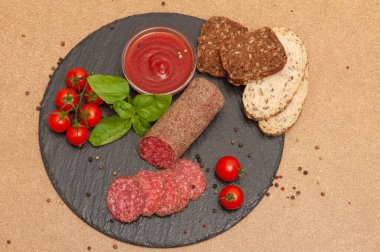 Soslu füme sosis, vişneli domates ve siyah grafit tahtasında ekmek dilimlenmiş fesleğen. en üstteki görünüm