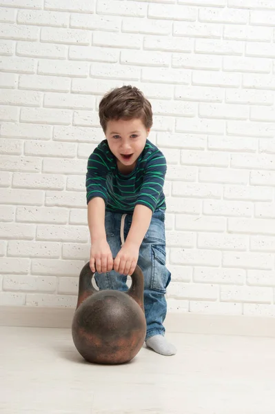 Pequeño niño intenta levantar un hervidor de agua de hierro — Foto de Stock